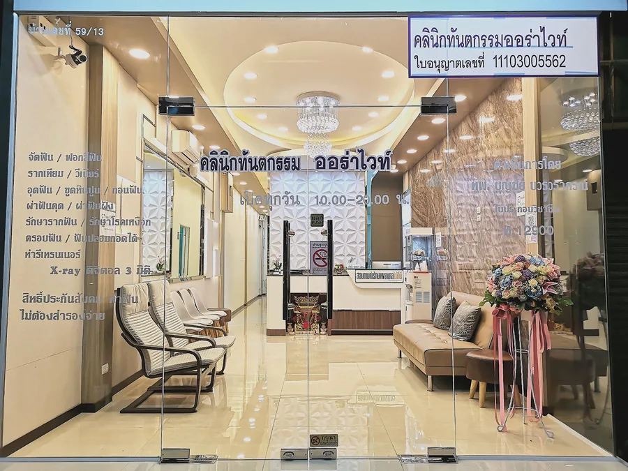 หน้าร้านคลินิกกระจกใส เห็นห้องรอ เคาน์เตอร์ต้อนรับ และเลขที่ใบอนุญาตประกอบกิจการ คลินิกทันตกรรม AuraWhite บางพลี
